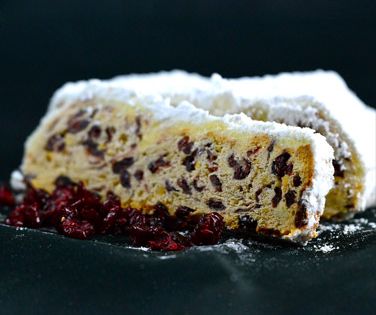Angeschnittener Cranberry-Stollen mit einer einzelnen Scheibe und einigen Cranberries im Vordergrund