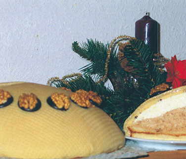 Lübecker-Nuss-Sahnetort – Unter einer Schicht aus Lübecker Marzipan verstecken sich hier, umhüllt von feinem Bisquit, zwei verschiedene Sahnesorten. Die kräftige Nougatsahne mit Haselnussstückchen konkuriert mit dem Geschmack der Marzipansahne. Jedes Stück wird gekrönt von einer halben Walnuss auf einem Schokoladenspielgel. Diese Torte enthält Alkohol.